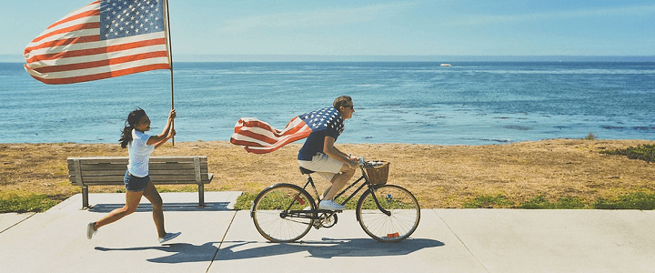 man wearing american flag riding bike with woman chasing and holding american flag