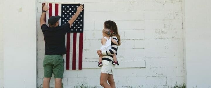man hanging american flag on wall while woman and baby look on