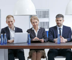 Stock photo of men and women sitting behind table staring at camera