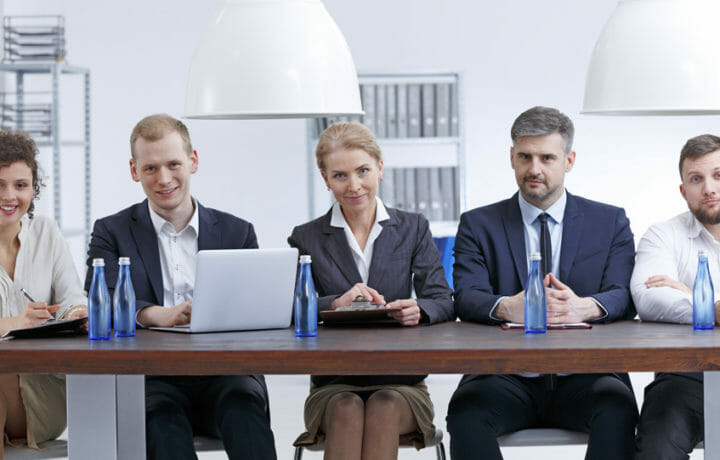 Stock photo of men and women sitting behind table staring at camera