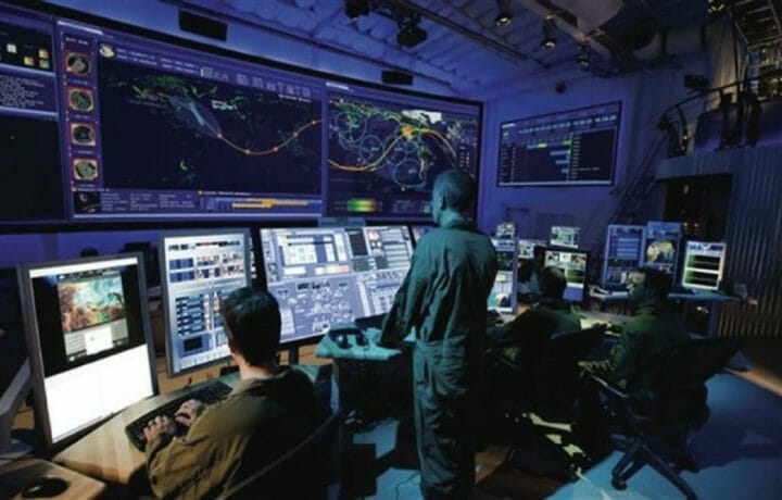 People in uniform standing in command center looking at screens