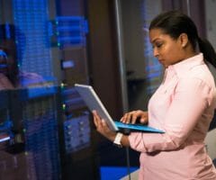 Woman standing and working on laptop near server racks