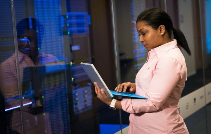 Woman standing and working on laptop near server racks