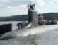 Submarine in water with tugboats and people standing on top