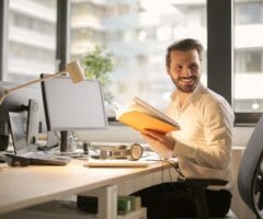 Man at desk with notebook smiling over shoulder