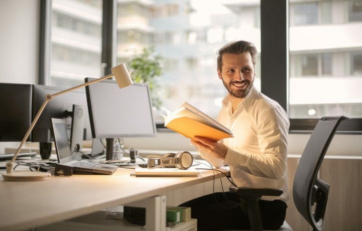Man at desk with notebook smiling over shoulder