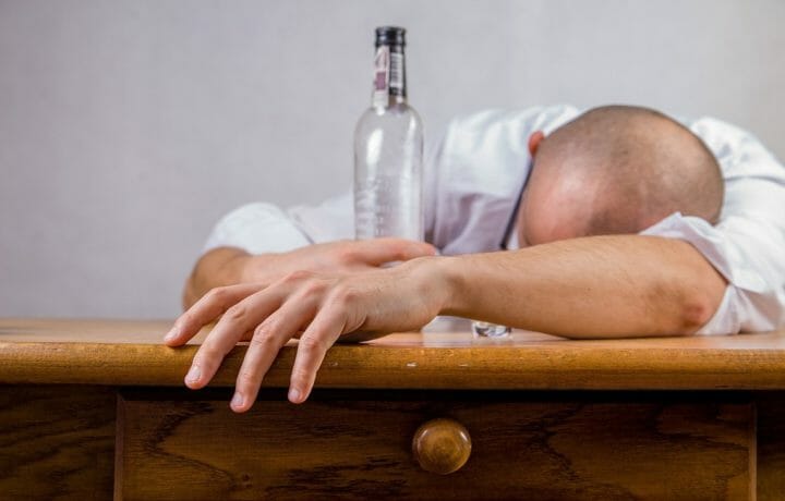 Man passed out on desk with bottle of alcohol