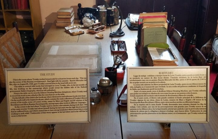 brown wood desk with antique books and signs in english and spanish side by side explaining the murder of Leon Trotsky