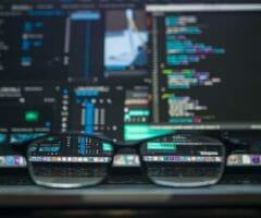 Photo of glasses sitting on desk with computer code in background