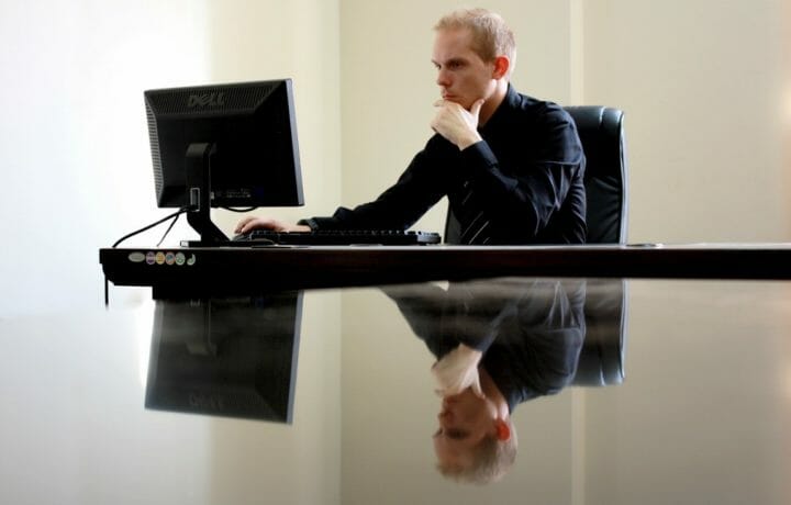 Man staring at computer screen reflected in shiny table