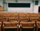Empty classroom chairs in front of dais and chalkboard