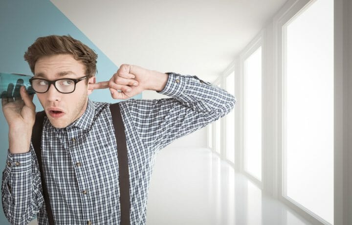 Man in glasses eavesdropping with glass on wall plugging ear