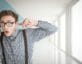 Man in glasses eavesdropping with glass on wall plugging ear
