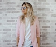 Woman in pink jacket leaning against white brick wall
