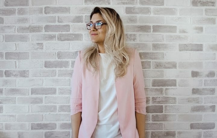Woman in pink jacket leaning against white brick wall