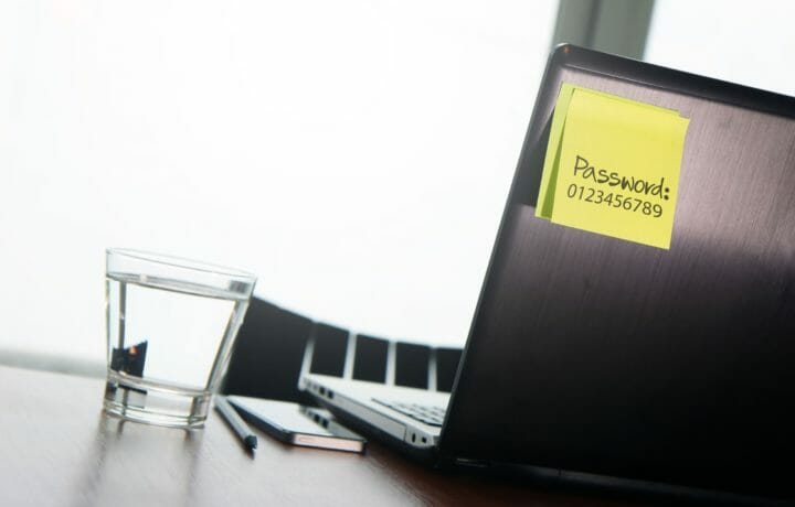 laptop on a desk with yellow sticky note with "Password: 1234567" written on it