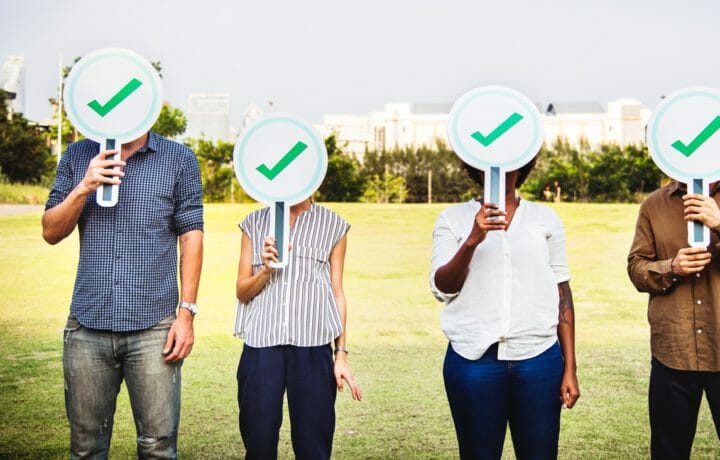 Four people with green check signs covering face