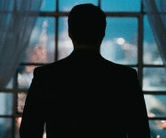 silhouette of a mysterious man in front of a window looking at a city at nighttime