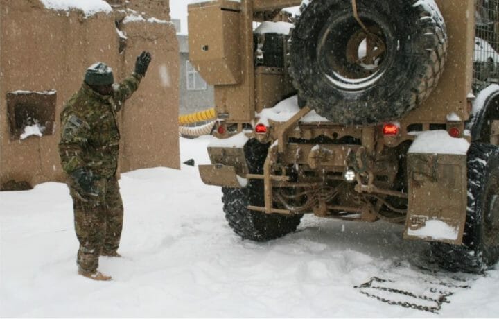 Sgt. Shaheem Daily, a platoon sergeant in Headquarters and Headquarters Battery, 3rd Battalion, 16th Field Artillery Regiment, 2nd Brigade Combat Team, 4th Infantry Division, guides a vehicle to back up onto snow chains Nov. 8. The day after receiving six inches of snow, the HHB had to travel north to pick up supplies. In order to make sure the trip was safe, they put snow chains on all the tires.