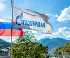 Russian national flag and Gazprom flag against a background of a sky and mountains.