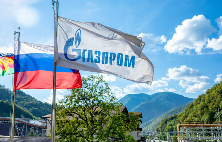 Russian national flag and Gazprom flag against a background of a sky and mountains.