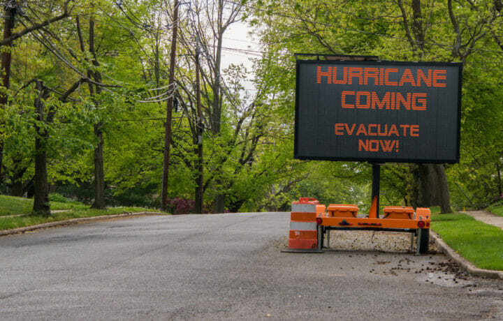 Hurricane Coming Evacuate Now warning information sign on trailer with LED face on suburban street lined with trees