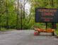 Hurricane Coming Evacuate Now warning information sign on trailer with LED face on suburban street lined with trees