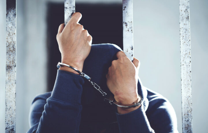 imprisoned man in handcuffs behind prison bars
