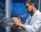 Side view portrait of young man in lab coat taking out blade server out of cabinet while working with supercomputer