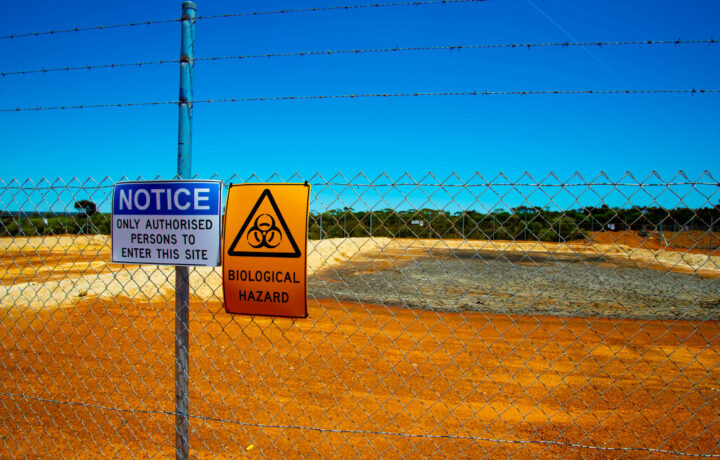 Photo of a fenced in area with two signs reading: NOTICE ONLY AUTHORISED PERSONS TO ENTER THIS SITE and BIOLOGICAL HAZARD