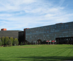 Photo of the University of Dayton Research Institute. Glass building with a green field and flags in front of the building.