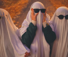 Three people dressed up as ghosts with sunglasses on. Middle ghost has their hands on their face.