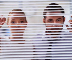 Two people looking through blinds.