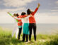 Four women with their backs to the camera, arms around each other facing the ocean and sky.