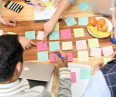 Photo of people around a table with a bunch of post-it notes on it.