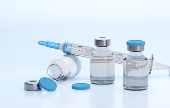 Photo of vaccine vials and syringe against a bluish-white background.