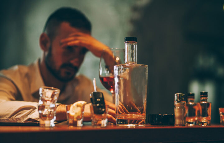 Photo of a man with his head in his hand, bottles of alcohol are in front of him.