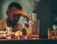 Photo of a man with his head in his hand, bottles of alcohol are in front of him.