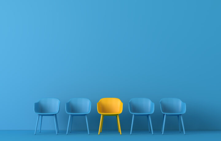 Image of blue chairs against a blue background, but in the middle is a yellow chair.