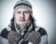 A man bundled in thick winter clothing with icicles hanging from his beard and mustache, crossing his arms and shivering, symbolizing being frozen or stuck.