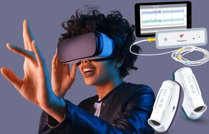 A person wearing a virtual reality headset and reaching out with one hand, accompanied by a connected device labeled "freespira" with cables and a tablet displaying graphs, alongside two handheld white electronic devices with buttons.